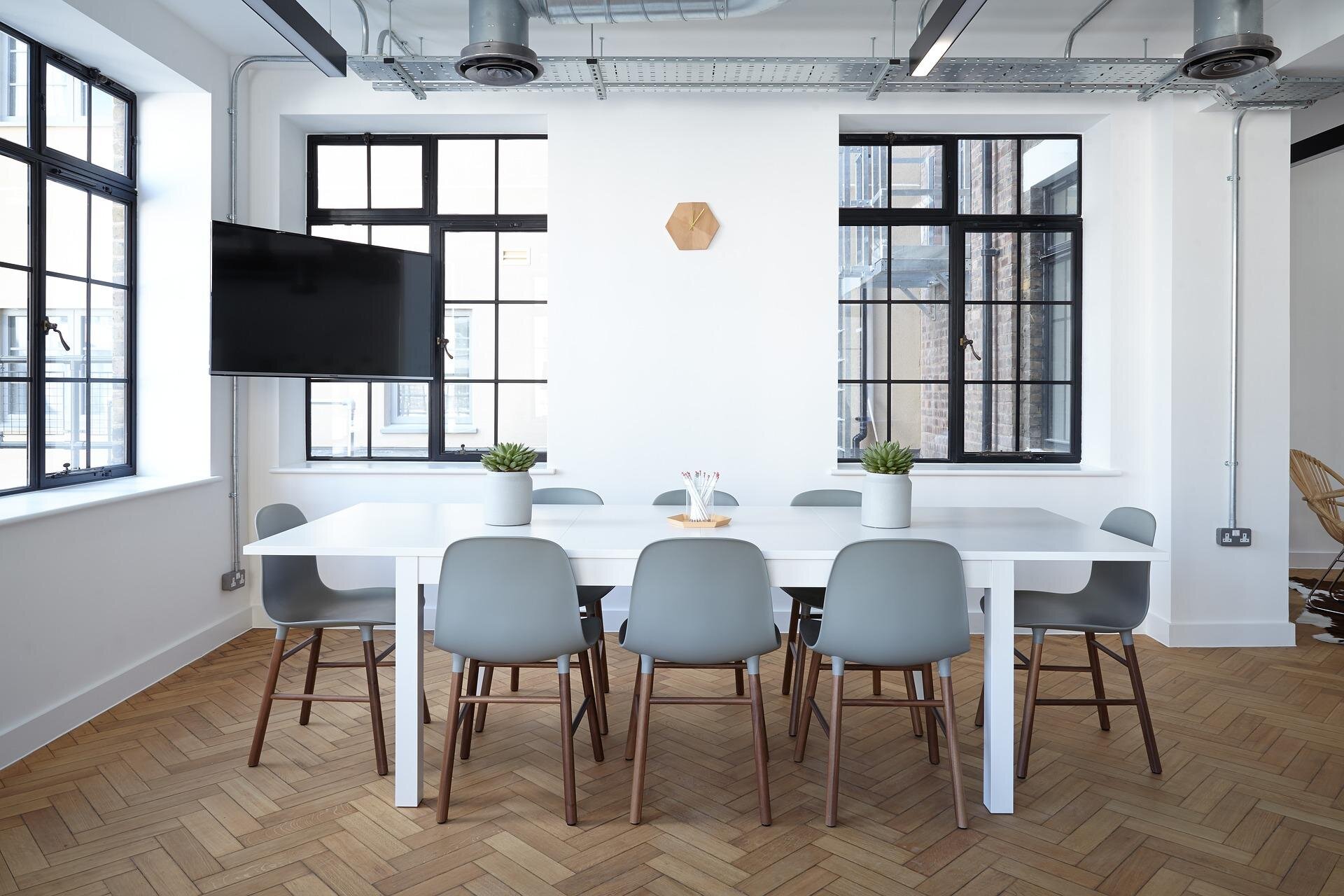 A bright, modern meeting room with a white table and wooden chairs