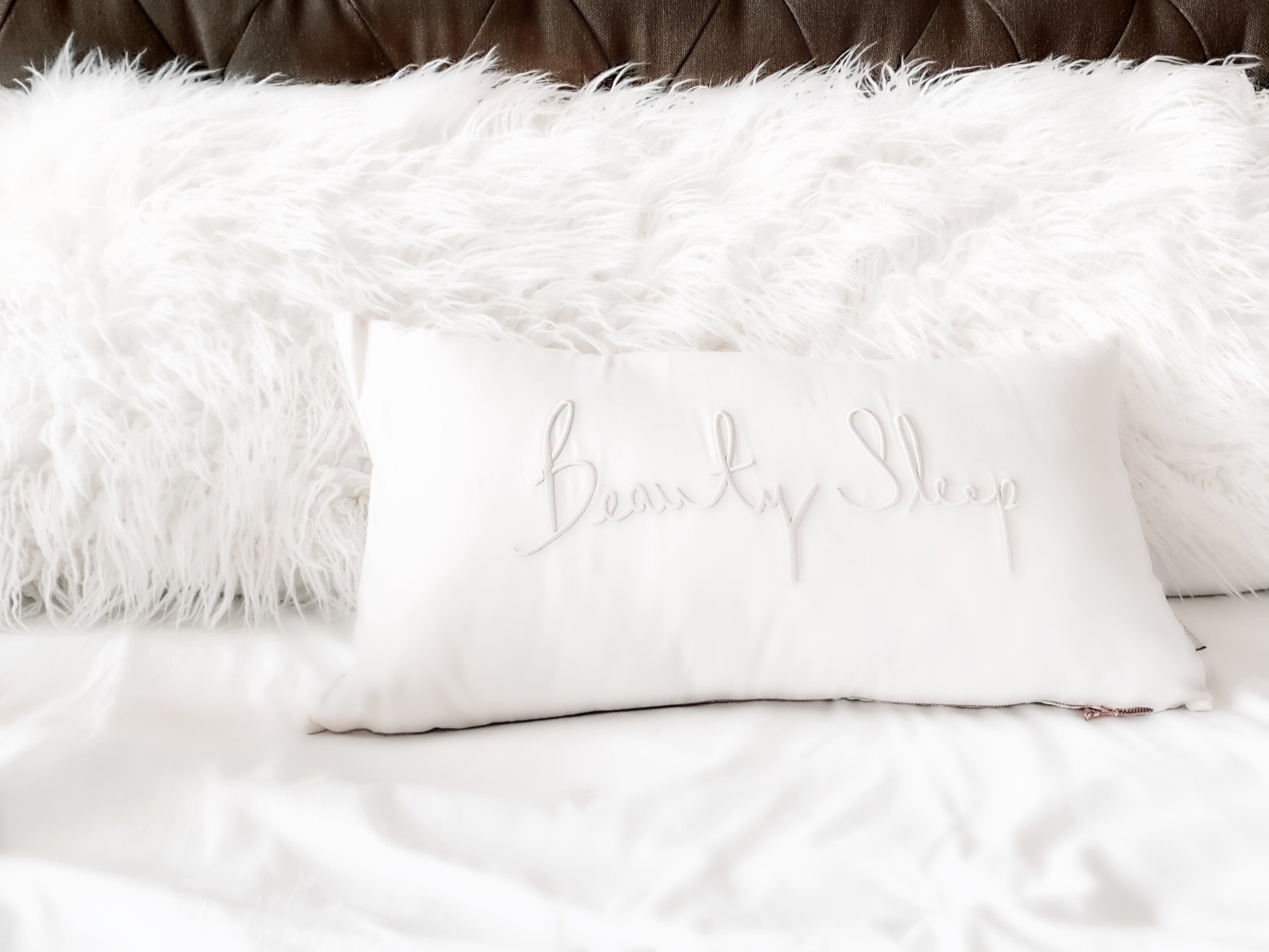 A white throw pillow embroidered with the words Beauty Sleep